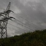 Electricity tower behind a green hill with a gray sky